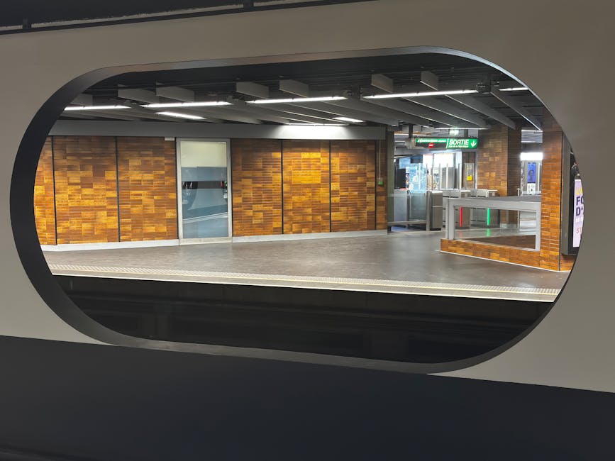 Interior of a London Underground station platform featuring a curved tunnels ceiling with white and grey tiles, illuminated by overhead linear lighting. The platform has a yellow safety line along its